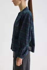 Blusa de calce relajado y silueta amplia, confeccionada en algodón liviano con estampado a cuadros en tonos azul marino y verde. Presenta cuello mao, cierre frontal con botones, hombros fruncidos y mangas largas con volumen que finalizan en puños elastizados.