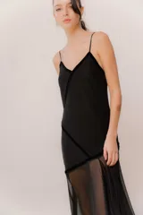 Vestido midi de color negro con diseño de breteles finos y escote delicado. Presenta una combinación de texturas con cuerpo en lycra y terciopelo, y una sobrecapa de microtul transparente en la parte inferior que aporta movimiento y fluidez.