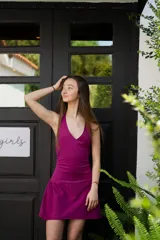 Vestido corto color fucsia con escote en V, breteles finos que se atan al cuello, corte a la altura de la cadera y falda acampanada con ruedo irregular.