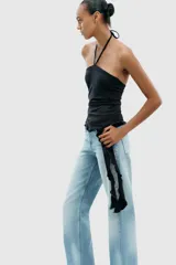 Top negro de cuello halter con lazada, escote recto y hombros descubiertos. Presenta un volante asimétrico en el lateral.