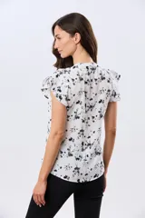 Blusa blanca sin mangas con volados en los hombros, cuello redondo con aberturas y cierre frontal parcial con botones.