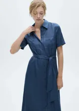 Vestido midi de estilo camisero en tejido satinado fluido, color azul. Presenta cuello camisero, cierre frontal con botones, mangas cortas con dobladillo y dos bolsillos de parche en el pecho. Incluye un lazo ajustable en la cintura para entallar la silueta.