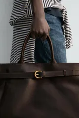 Bolso de mano de piel marrón oscuro de alta calidad con detalle de cinturón decorativo con hebilla metálica dorada y dos asas cortas.