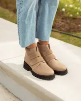 Botín corto de cuero color visón (beige/topo), con cierre de tres tiras de velcro en el empeine. Posee cuello acolchado de gamuza y suela de goma negra con relieve tractor.