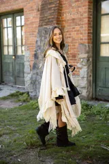 Ruana de tejido liviano color beige, con diseño abierto y detalles de volados en mezcla de lino y algodón. Presenta terminaciones con flecos en el ruedo y cordones decorativos con borlas en el frente.