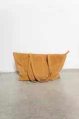 Bolso tipo tote de gamuza color tostado, con doble asa de hombro y cierre superior con cremallera.