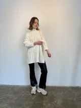 Sweater tejido en lana italiana con alpaca y viscosa, color crudo, con cuello alto y mangas largas. Diseño con trenzas en el frente y mangas. Corte holgado.