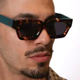 Lentes de sol con armazón de diseño rectangular y estampado carey. Presentan patillas en color verde petróleo con detalle metálico de la marca.