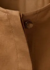 Chaqueta de diseño corto en tono tostado, confeccionada con mezcla de lyocell, algodón y lino. Presenta cuello redondo, mangas largas abullonadas, elásticos en los laterales y cierre frontal de botonadura visible.