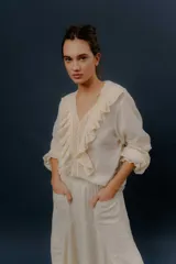 Camisa blanca de algodón con escote en V, volados delanteros y detalles de encaje en el frente y las mangas.