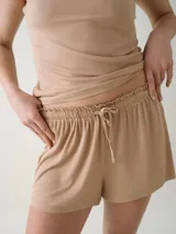 Short de dormir color beige, confeccionado en tejido rib, con cintura elastizada, cordón ajustable y detalle de volados en la parte superior.