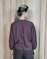 Camisa de manga larga con diseño de rayas verticales y bordados sutiles. Presenta cuello redondo, cierre frontal con botones y mangas abullonadas con volados en los hombros.