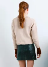 Chaqueta de punto color beige, de corte corto, con cuello camisero, bolsillos frontales con solapa y botones metálicos.