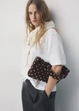 Bolso de hombro tipo baguette confeccionado en piel bovina color marrón oscuro, con diseño estructurado y superficie decorada con tachas metálicas plateadas distribuidas uniformemente. Cuenta con cierre superior y asa integrada.