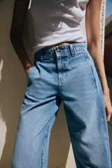 Jeans de tiro medio con pernera holgada tipo barrel que se estrecha hacia el tobillo, acabado con bajo sin costura, bolsillos delanteros y bolsillos de plastrón en la espalda. Cierre frontal con cremallera y botón.