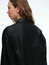 Chaqueta camisera de corte oversize en color negro, confeccionada en cuero sintético. Presenta cuello clásico, cierre frontal con botones y mangas largas con puños abotonados.