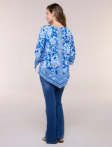 Blusa de gasa azul con estampado floral y geométrico estilo pañuelo, escote redondo, mangas tres cuartos amplias con jareta ajustable y ruedo asimétrico en punta.