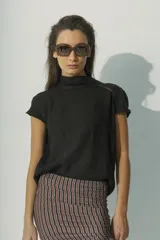 Blusa de lino color negro, con cuello alto y mangas cortas con detalle de costura decorativa en los hombros. Presenta un diseño minimalista de silueta recta y tejido liviano.