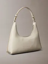 Cartera de hombro Calvin Klein de diseño estructurado en color beige, con cierre de cremallera superior, correa ajustable y detalle del logo de la marca grabado en la parte frontal.