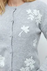 Cardigan de punto color gris melange con cuello redondo, cierre frontal de botones y delicado bordado floral en color blanco en la parte frontal.