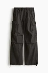 Pantalón estilo parachute de corte holgado, color negro, con cintura elástica ajustable mediante cordón, bolsillos cargo laterales con solapa, bolsillos traseros y cordón ajustable en los tobillos.