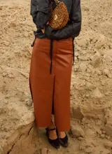 Falda larga de cuero color mostaza, de tiro bajo y silueta recta con tajos delanteros y laterales, bolsillos funcionales y cierre de botón.