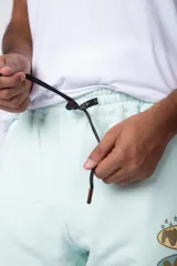 Pantalón jogger de corte oversize confeccionado en tela rústica color verde agua claro. Presenta una estampa gráfica localizada en el muslo izquierdo con diseño de óvalos y estrellas.