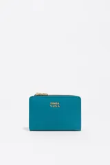 Billetera compacta de estructura blanda en color turquesa, con cierre de cremallera superior y logo metálico dorado en el frente.