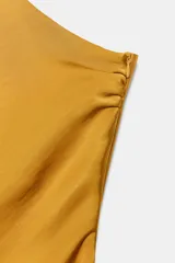 Vestido midi de satén color mostaza con escote asimétrico de un solo hombro y corte evasé. Presenta pliegues en el hombro y cierre lateral con cremallera oculta.