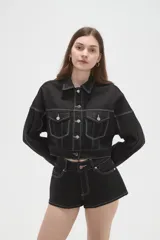 Campera corta de jean color negro con costuras a contratono en blanco, bolsillos frontales con solapa y cierre de botones metálicos.