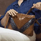 Bandolera marrón con paneles de cuero liso, cuero texturizado y gamuza. Tiene correa de mano y correa larga ajustable y removible.