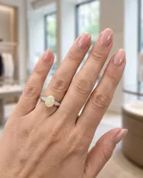 Anillo de plata con ópalo blanco ovalado en el centro, flanqueado por pequeños detalles de circonias en el aro.