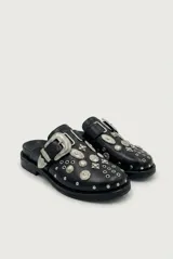 Mocasín de cuero sintético negro con suela plana, detalle de gran hebilla metálica plateada y apliques de tachas y condecoraciones metálicas de estilo western en el empeine.