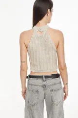 Top de punto estilo halter, color crudo, con cuello alto ajustado, diseño sin mangas y corte corto.