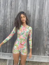 Traje de baño enterizo de lycra reciclada con estampado de flores y cactus en tonos rosa, verde y naranja. Tiene mangas largas, cierre en la espalda y protección SPF 50.