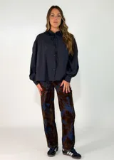 Camisa negra de corte holgado con cuello tipo bebé con volados y lazo de ajuste, cierre frontal con botones y mangas largas abullonadas con puños abotonados.