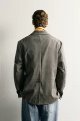 Blazer de corte relaxed fit confeccionado en 100% lana, con diseño de cuadros grises y marrones, solapas de pico, bolsillos de parche en la cadera y cierre frontal de un botón.
