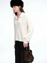 Sweater de tejido de punto color beige, con diseño de trenzas en el frente y mangas lisas. Presenta cuello polo con escote en V y puños y ruedo acanalados.