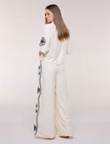 Conjunto de dos piezas negro compuesto por camisa de manga corta con cuello camisero y pantalón palazzo de tiro alto. Presenta detalles de bordados florales en contraste a lo largo de los laterales del pantalón y en las mangas.