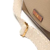 Bandolera de material símil cuero color taupe, con solapa frontal redondeada y cierre superior. Posee correa larga regulable y desmontable, y herrajes metálicos dorados. Lleva un logo metálico de la marca XL aplicado al frente.