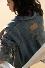 Vestido camisero corto de denim azul, con cuello camisero, cierre frontal con botones y mangas largas con puños abotonados.