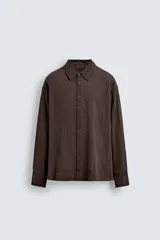 Camisa de corte relajado confeccionada en tejido ligero de algodón con textura de cuadros. Presenta cuello solapa, manga larga con puños abotonados y cierre frontal de botones.