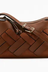 Cartera marrón con diseño tejido en la parte frontal, cierre superior y correa ajustable con hebilla metálica.