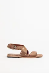 Sandalias bajas de cuero negro con tachas plateadas, tiras cruzadas y hebilla al tobillo.