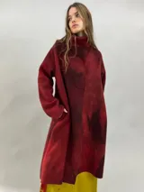 Tapado de lana merino afieltrada con diseño artesanal teñido en tonos violeta y fucsia. Presenta cuello elevado, cierre frontal con broches ocultos, bolsillos laterales y un corte ligeramente más largo en la parte trasera.