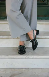 Sueco de cuero color borgoña con cordones, ojales y hebillas plateadas. Tiene tira trasera regulable con elástico.