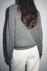 Jersey de punto color gris, con cuello redondo y abertura frontal con botones. Presenta mangas largas raglán y puños y bajo acanalados.