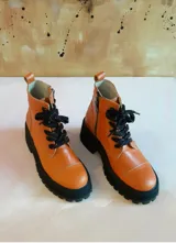 Borcego de cuero color naranja de caña media, con suela de plataforma y taco grueso negro, cordones oscuros y cierre lateral.