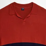 Remera de punto de manga corta con cuello polo, diseño bicolor que combina un tono rojizo en la parte superior y azul marino en la parte inferior.
