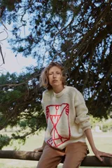 Sweater de lana color crudo con diseño gráfico bordado en color rojo en el frente. Presenta cuello redondo, mangas largas y puños acanalados.